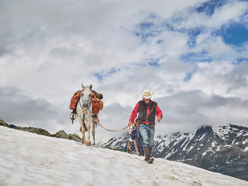 Reiter führt ein weißes Pferd durch Schnee in den Alpen