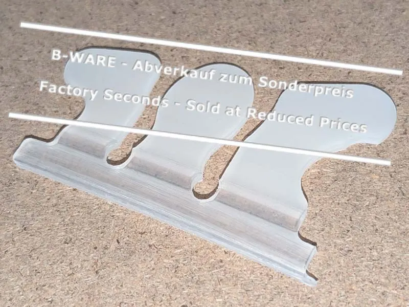 Eine aussortierte Wolf Busch Basic Klebelasche liegt auf einer Werkbank. Die Lasche hat nicht ganz die richtige Form, ist aber funktionell in Ordnung und wird daher zum Sonderpreis verkauft.