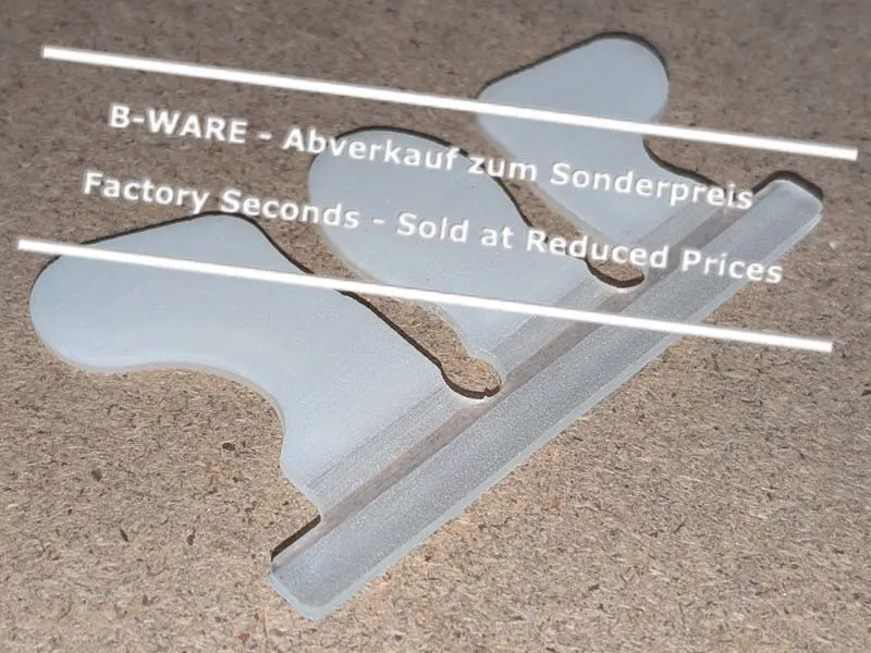 Eine aussortierte Wolf Busch Basic Klebelasche liegt auf einer Werkbank. An der Lasche befindet sich die kleine Wölbung nicht an der richtigen Stelle. Sie ist aber funktionell in Ordnung und wird daher zum Sonderpreis verkauft.