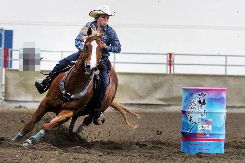 Reiterin beim Barrel Racing reitet um eine blaue Tonne.