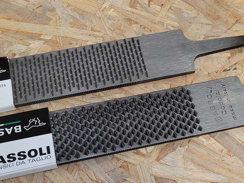 Die Bassoli Doppia Hufraspel liegt auf einer Holzplatte; es sind beide Seiten sichtbar, die Raspel- und die Feilenseite.