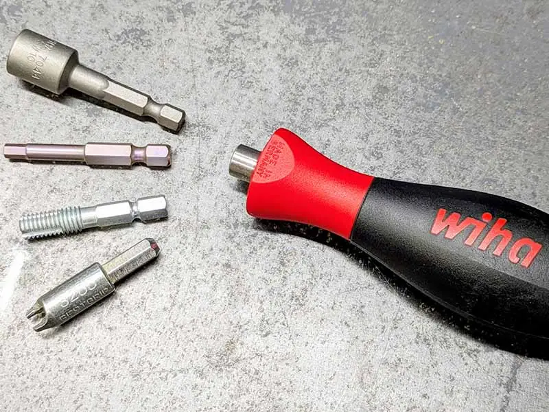 Der wiha Bithalter liegt gemeinsam mit verschiedenen Biteinsätzen zur Spike uns Stollenmontage beim Hufeisen auf einer Metallplatte.