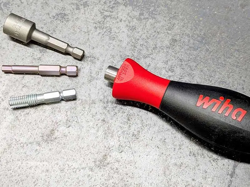 Der wiha Bithalter liegt gemeinsam mit verschiedenen Biteinsätzen zur Stollenmontage beim Hufeisen auf einer Metallplatte.