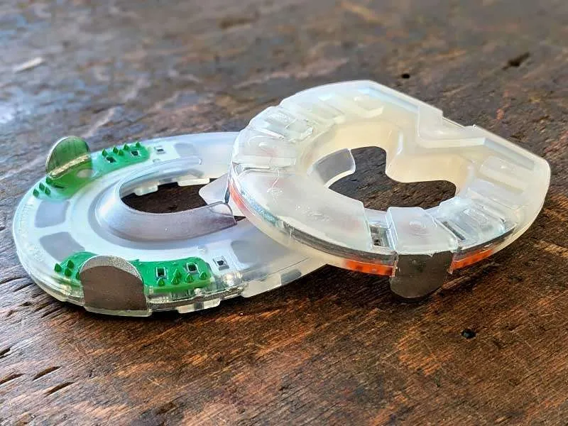 Un fer de poids de pince avec une enveloppe synthétique et un renforcement en acier est posé sur une table en bois en deux variantes différentes.