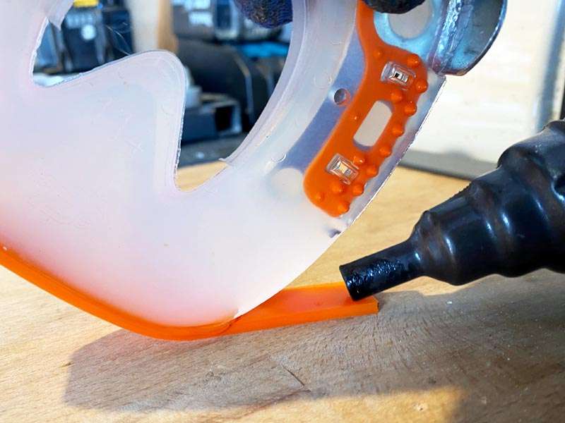 ein oranger Farbstreifen wird mit einem Heißluftapparat an einen Kunststoff-Hufbeschlag geschweißt