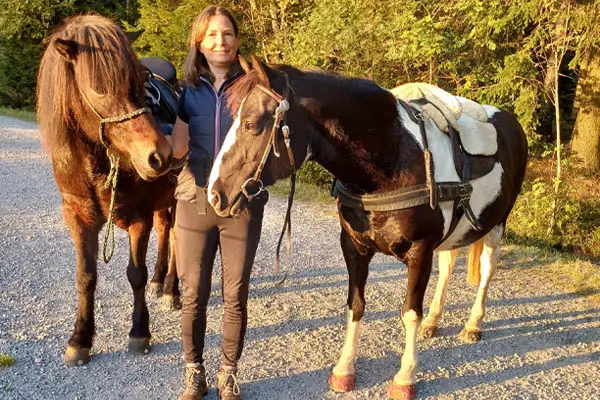 Pferdebesitzerin steht mit ihrem deutschen Reitpony-Mix und ihrem Islandwallach auf einerm Schotterweg im Bayerischen Wald.