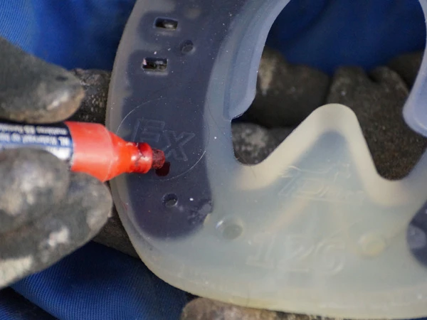 Der Hufschmied markiert die geplante Position des Stollenlochs am Hufeisen mit einem roten Permanentmarker.