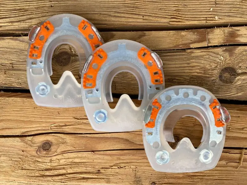 Die Verbundhufeisen mit Seitenkappen und Gewinde in den verschiedenen Formen rund und gerade Zehe für Vorderhufe und oval für die Hinterhufe des Pferdes liegen auf Holzbrettern