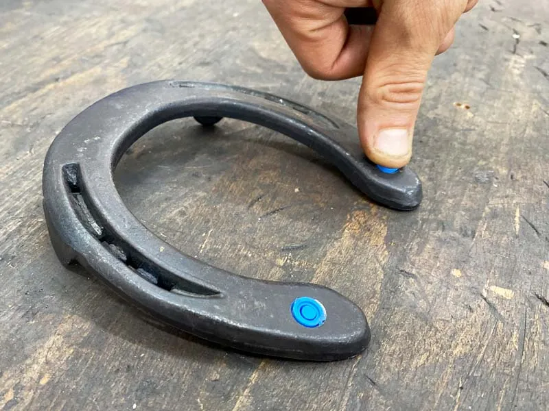 Someone presses a blue closure plug into the threaded hole of a steel shoe using their thumb.