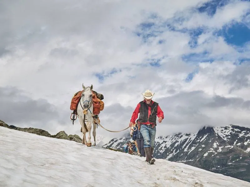 ein Wanderreiter führt sein Pferd im Schnee in den Alpen