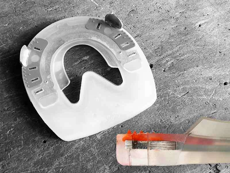 alternatives Hufeisen mit Kunststoffmantel und Strahlunterstützung liegt auf Holz; man sieht auch einen Querschnitt vom Aufbau Nagellochs im Hufeisen