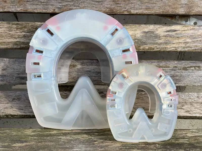 side by side, a small and large particularly solid synthetic horseshoe stand in front of a wooden wall