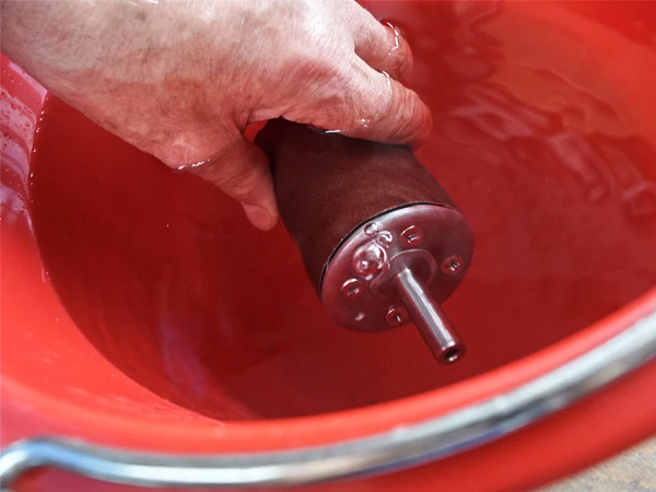 A fully assembled Hoof Buffer with the sanding belt fitted is held under water while air bubbles escape.