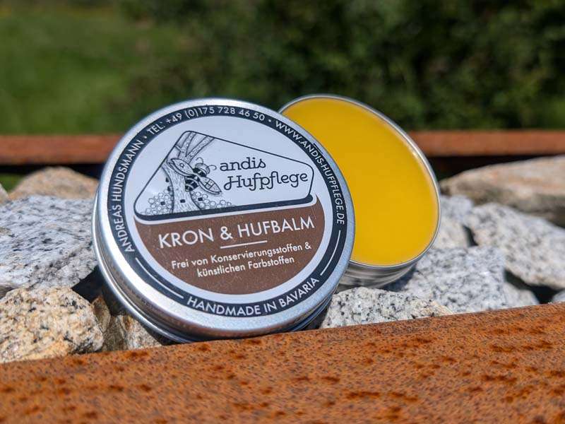 The can of Kron- und Hufbalm from Andis Hoof Care is open on stones in the garden, and the balm is yellow.