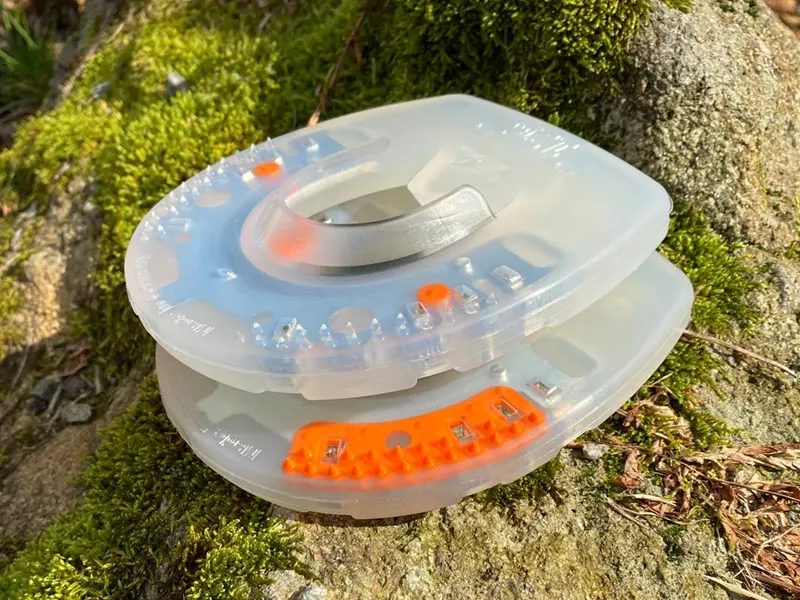 due ferrature con rivestimento in plastica senza barbette sovrapposte su una pietra coperta di muschio. In alto il modello Nailless senza inserto rigido, sotto un modello standard con inserto arancione.