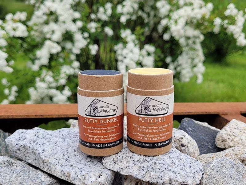 Putty hell und dunkel von andis Hufpflege stehen auf Steinen vor einem Blütenstrauch