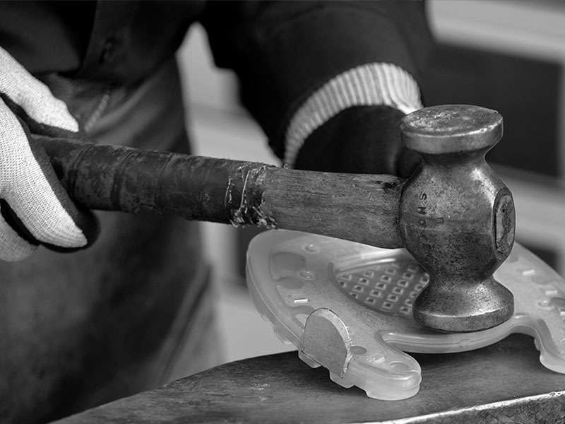 Der Hufschmied bearbeitet den mittleren Steg des zehenoffenen Verbundhufeisens mit dem Hammer.