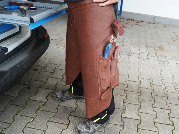 Un herrador lleva el delantal Elite largo de cuero completo en color marrón.