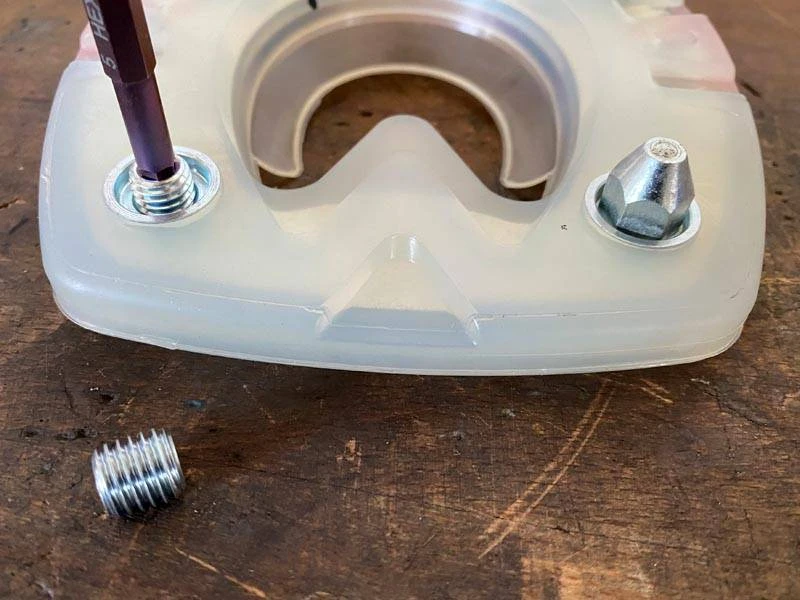 ein Verschlussstopfen aus Metall wird in ein Stollenloch eines Verbundhufeisens geschraubt