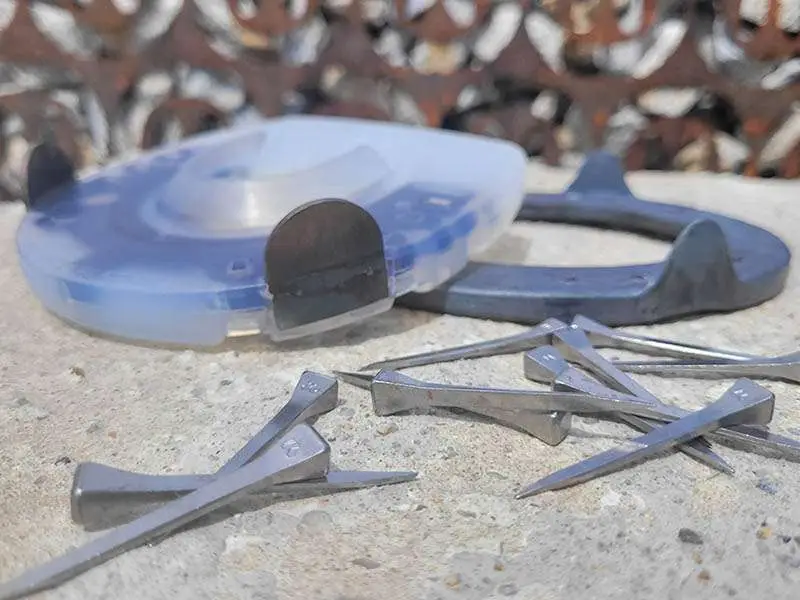 Symbolbild für genagelten Hufschutz - Mustad Hufnägel liegen auf einer Steinplatte vor einem Verbundhufeisen und einem Eisen.