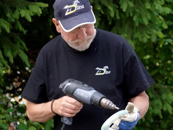 Ing. Hoerby Mende hält eine Verbundbeschlag in den Händen und bereitet diesen mit der Heißluftpistole zum Anschweißen der Klebelaschen vor.