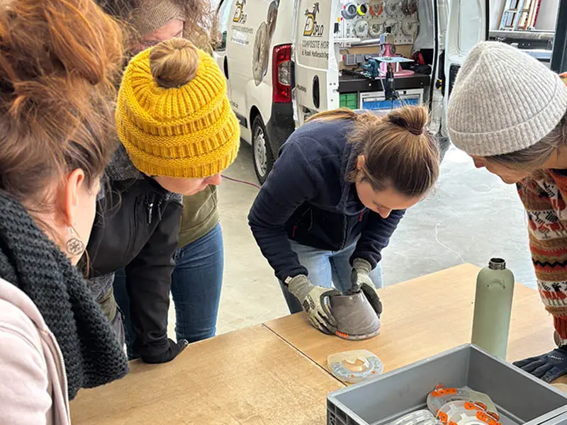 During the workshop on glue-on horseshoes, participants gather around the instructor and watch as she checks the fit of the horseshoe on the training hoof capsule.