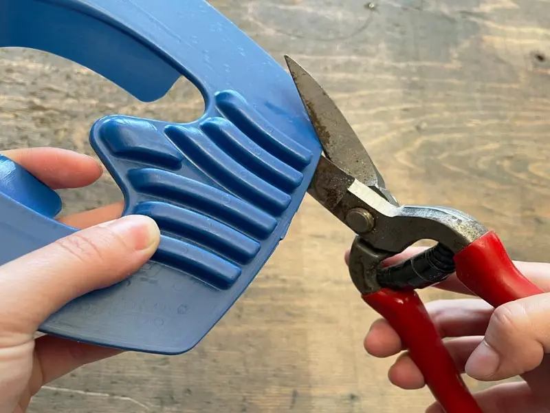 Dettaglio di una soletta in plastica blu per ferratura con supporto per il fettone, in fase di taglio con una cesoia per cuoio.