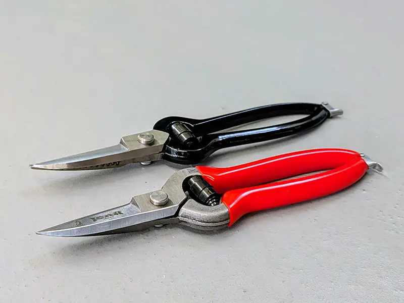 Image showing the black leather shears from Blacksmith and the red grip shears from ICAR lying side by side on a concrete floor.