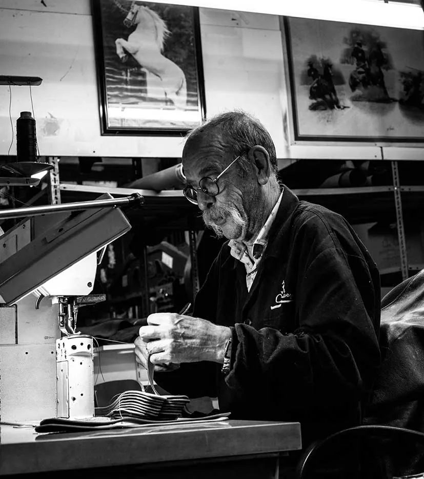 Foto en blanco y negro del maestro artesano de Con Cuero cosiendo un delantal para herrador.