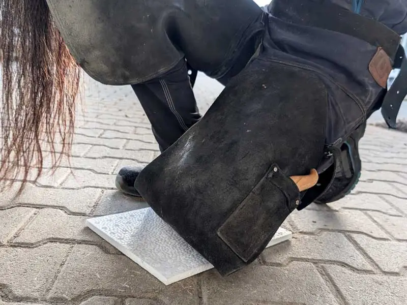 Durante il lavoro sullo zoccolo, il maniscalco è inginocchiato su una piastra ammortizzante bianca, per non poggiare direttamente sul terreno.