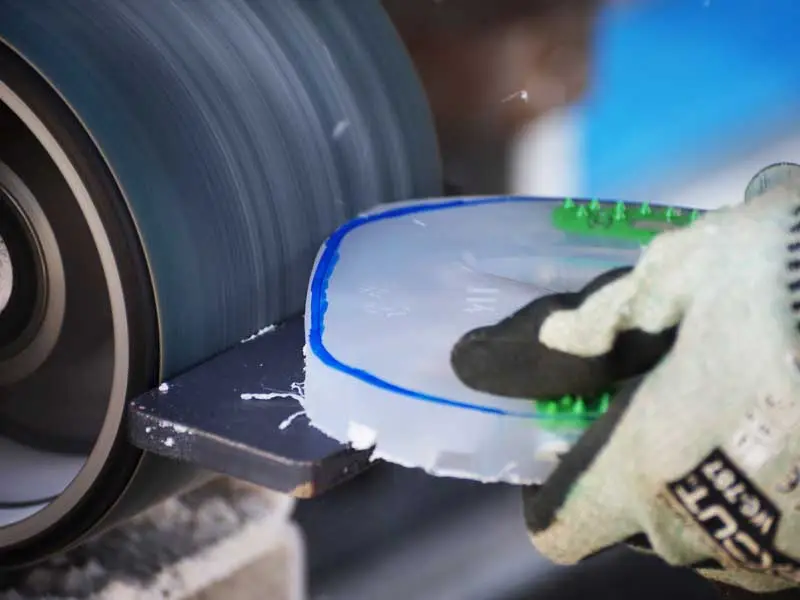 view of the farrier’s hands while adjusting an alternative hoof protection to the hoof shape of the client’s horse; a belt grinder is visible in the background