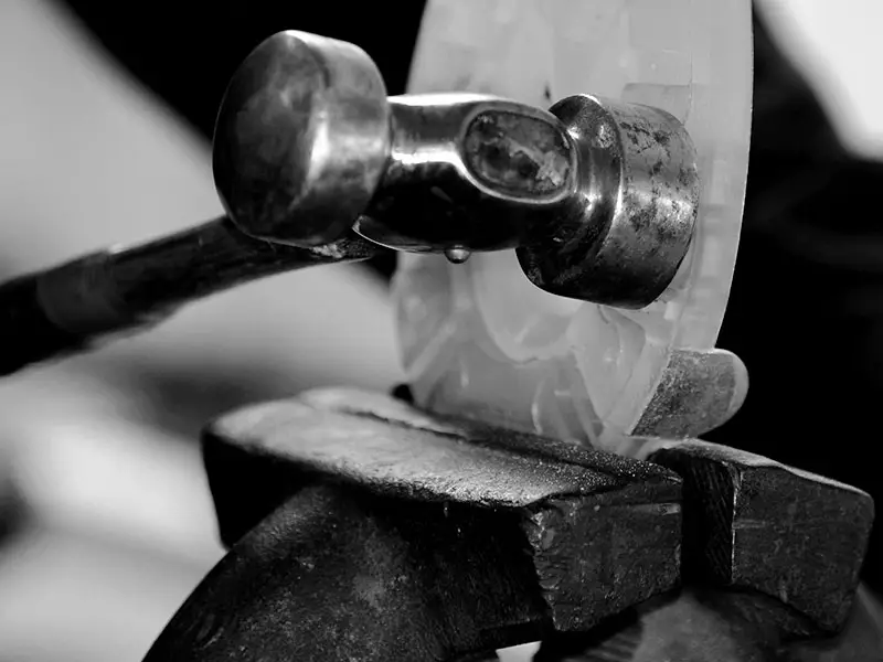 A composite horseshoe with a shock-absorbing plastic coating is clamped in a vise while the farrier uses a forging hammer to shape it to fit the horse's hoof.
