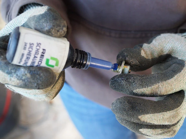 Detailaufnahme beim Auftragen von einem Tropfen EURO-LOCK Schraubensicherung auf einen Gleitschutz-Stollen für Verbund-Hufeisen