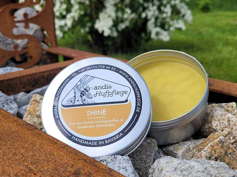 geöffnete Dose Shine von andis Hufpflege liegt auf Steinen