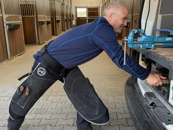 Un herrador prepara su vehículo de herraje móvil para un servicio. Lleva un delantal Hybrid Pro Chaps de Silverback.