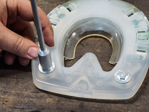 Un maréchal-ferrant visse un crampon avec collerette dans un fer composite pour chevaux.