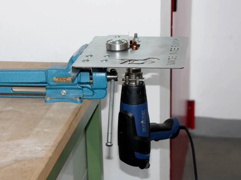 un appareil à air chaud de la marque Steinel est fixé sur un dispositif pour la fabrication de fers à cheval collés, qui est lui-même fixé dans un étau bleu clair