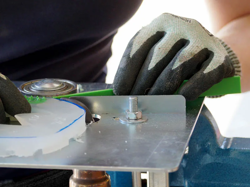 Les mains portant des gants de protection contre les coupures tiennent une ferrure en plastique et une bande de couleur verte lors du soudage à l'aide d'un dispositif spécial.