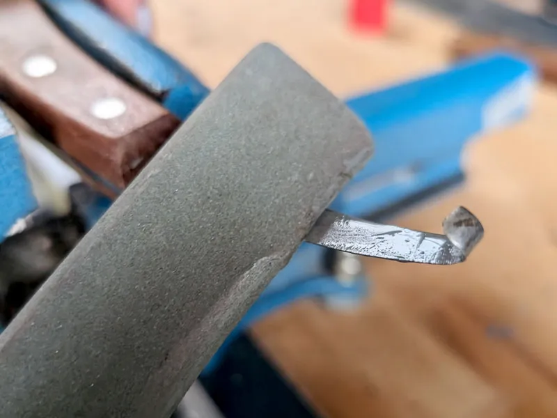 Farrier sharpening a hoof knife with a silicon carbide whetstone.